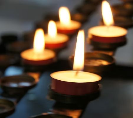 Close-up of several lit candles in a dark setting, with blurred background.