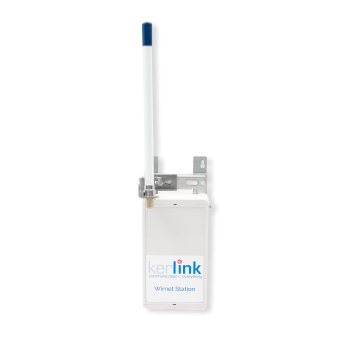 A white Kerlink Wirnet Station with a blue-tipped antenna mounted on a white wall bracket.