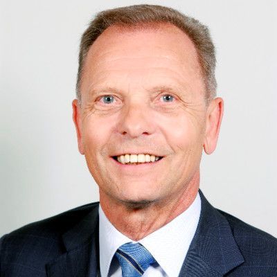 Man in pak lacht, tegen een lichtgrijze achtergrond.