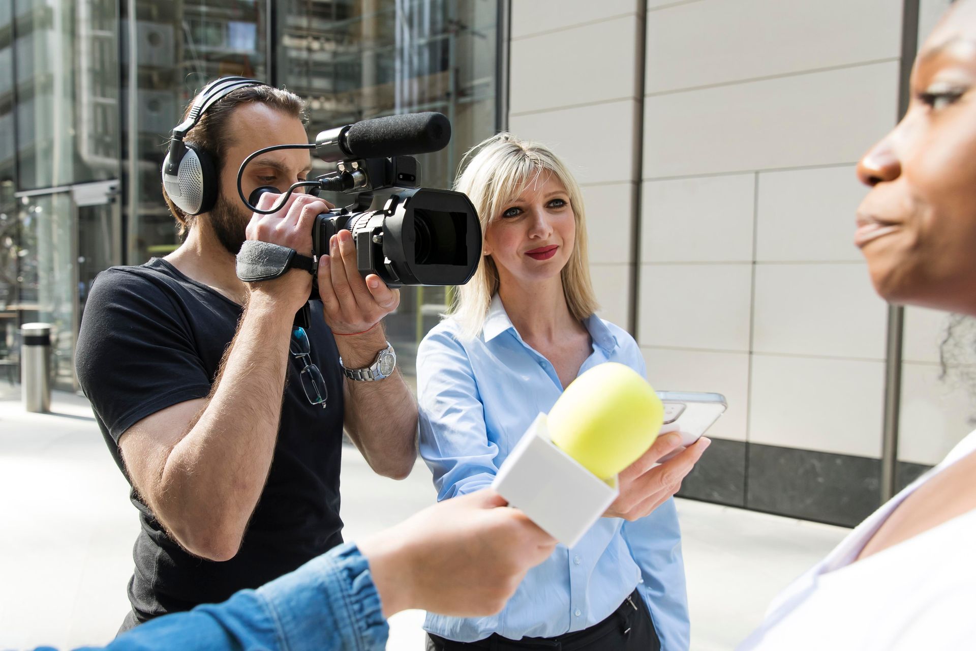Een cameraman filmt een vrouw die buiten wordt geïnterviewd, terwijl een andere vrouw een microfoon vasthoudt.