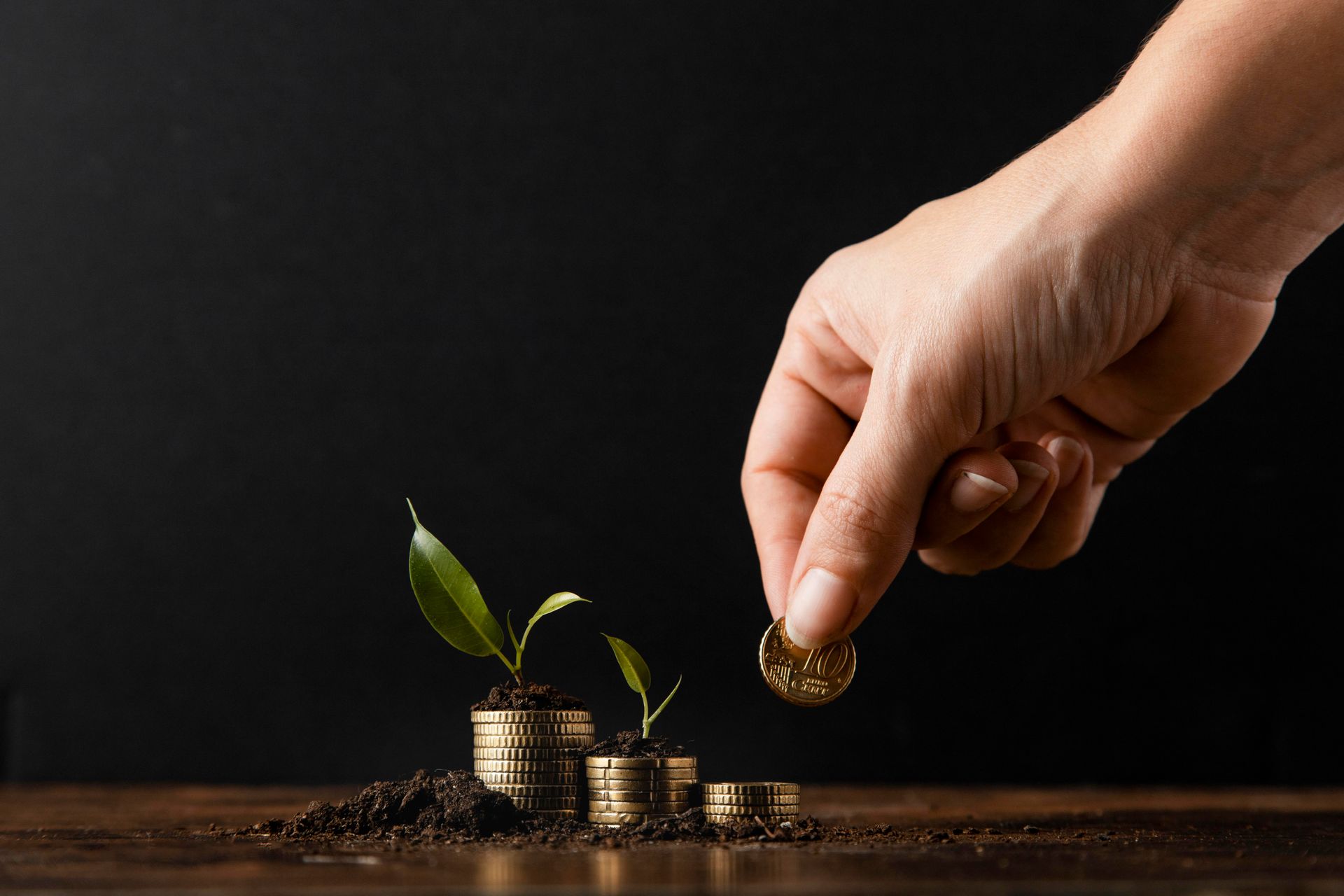 Hand die een munt op een groeiende stapel munten met planten legt; een investeringsconcept.
