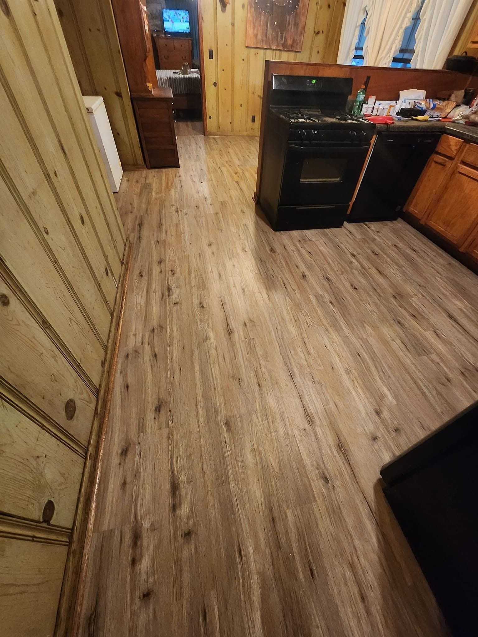 Kitchen floor with light wood-look vinyl, black appliances, and wood cabinets in a narrow hallway.