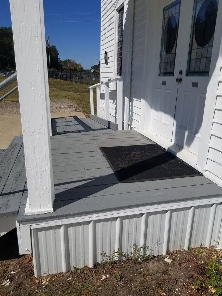White house front porch with ramp, white railings, and double doors in bright sunlight