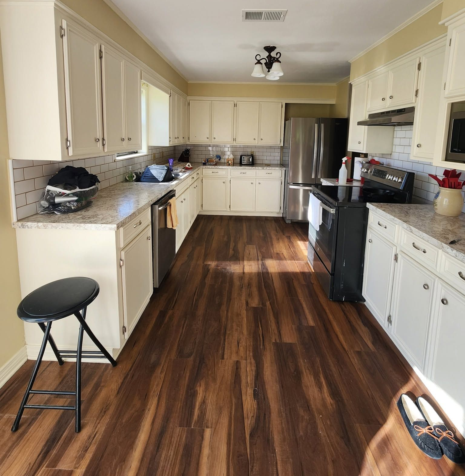 Bright kitchen with white cabinets, dark wood floors, and a black stool near the counter.