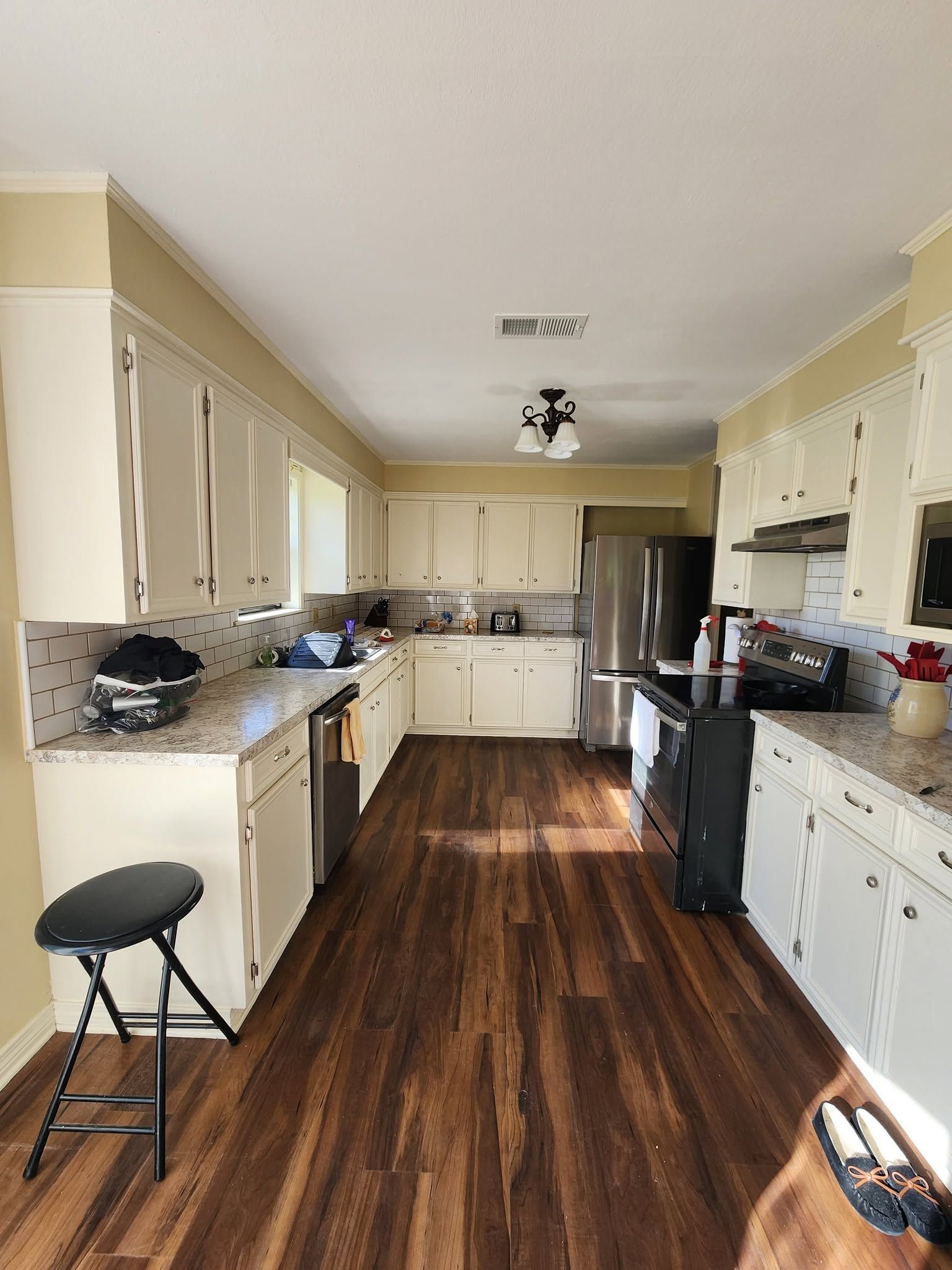 Narrow kitchen with cream cabinets, dark wood floor, and stainless steel refrigerator and oven.
