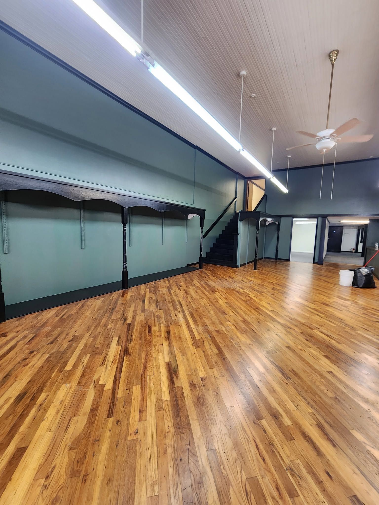Empty dance studio with wooden floors, mirrors, blue walls, and ceiling fans under bright lights