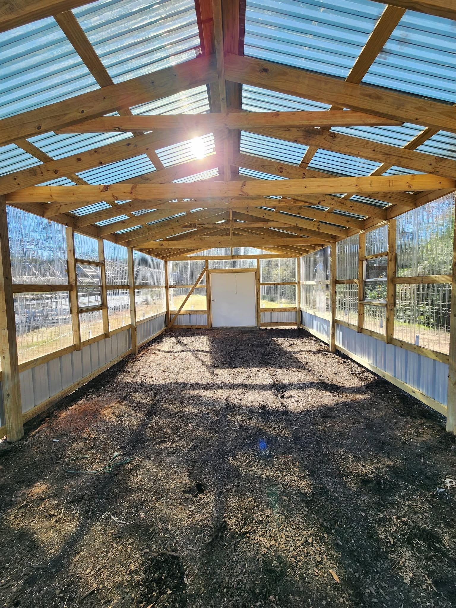 Empty wooden greenhouse with a gravel floor and sunlit slatted roof