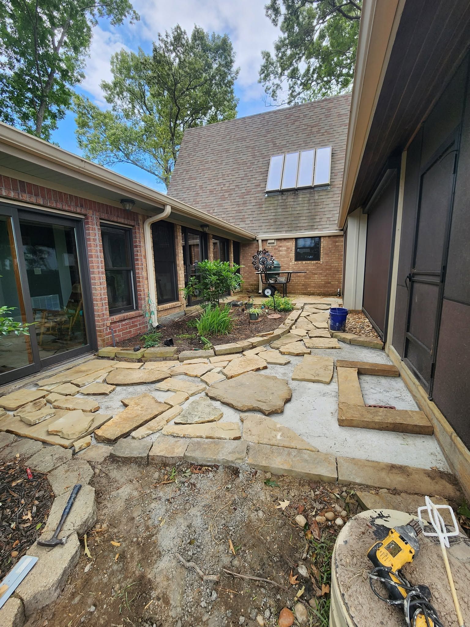 Backyard patio with stone pavers, a curved roof, trees, and a yellow tool in the foreground