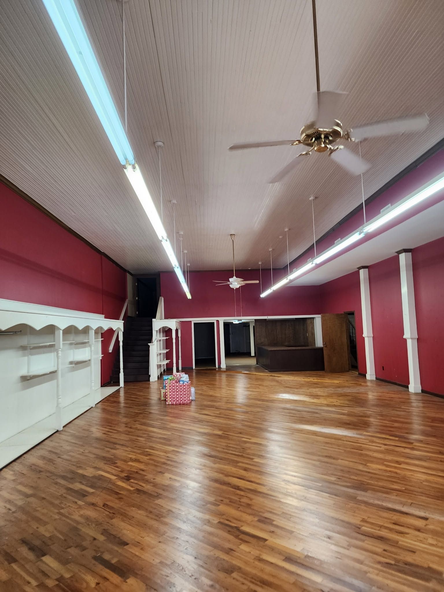 Empty dance studio with polished wood floor, mirrors, ceiling fans, and red walls.