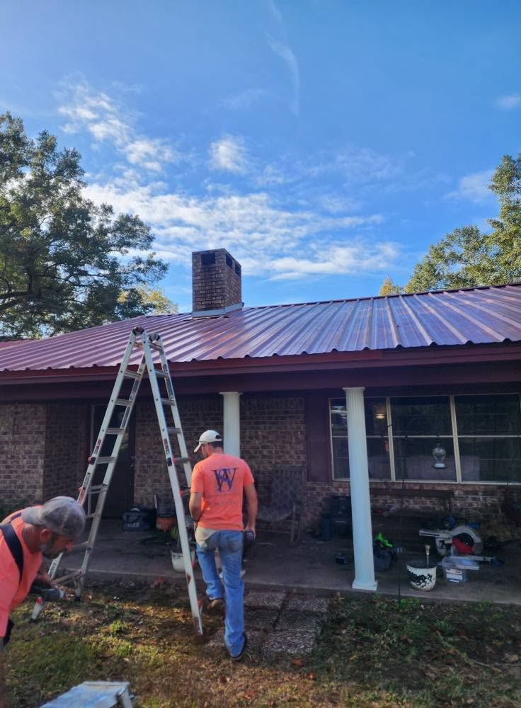 Workers on a ladder repairing a red metal roof on a house with a chimney