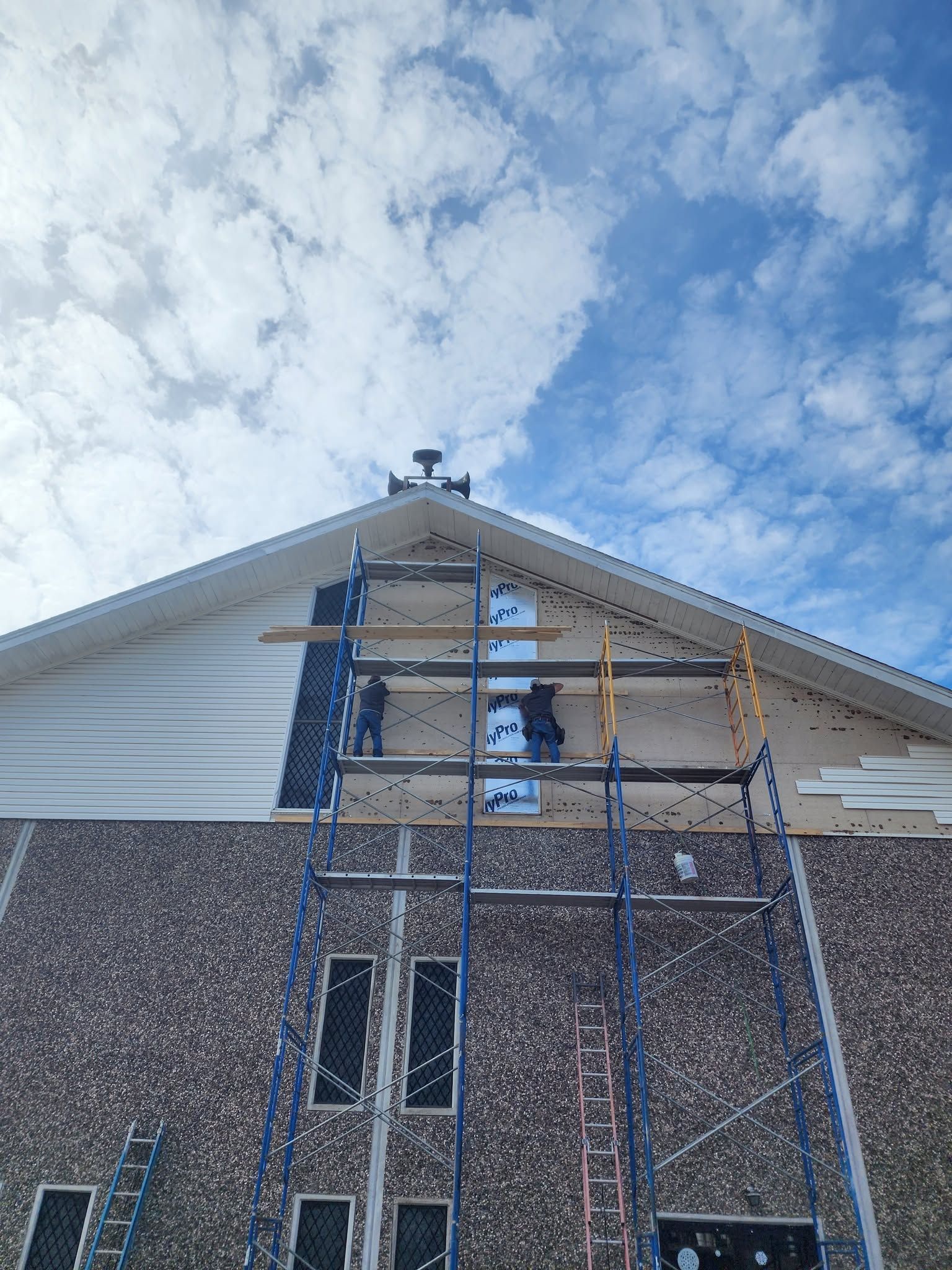 Person on blue scaffolding working on a house gable under a cloudy sky