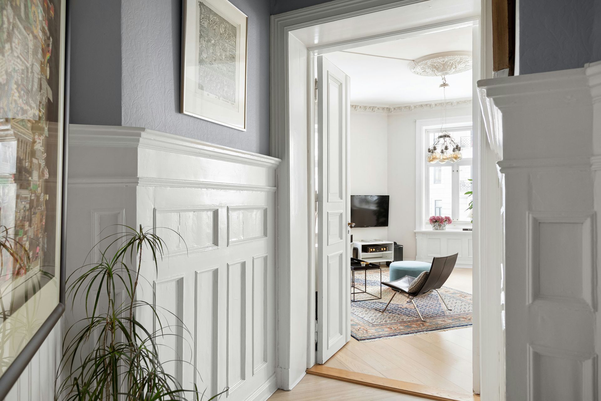 Hallway with white wainscoting leading into a bright living room with a rug and chair