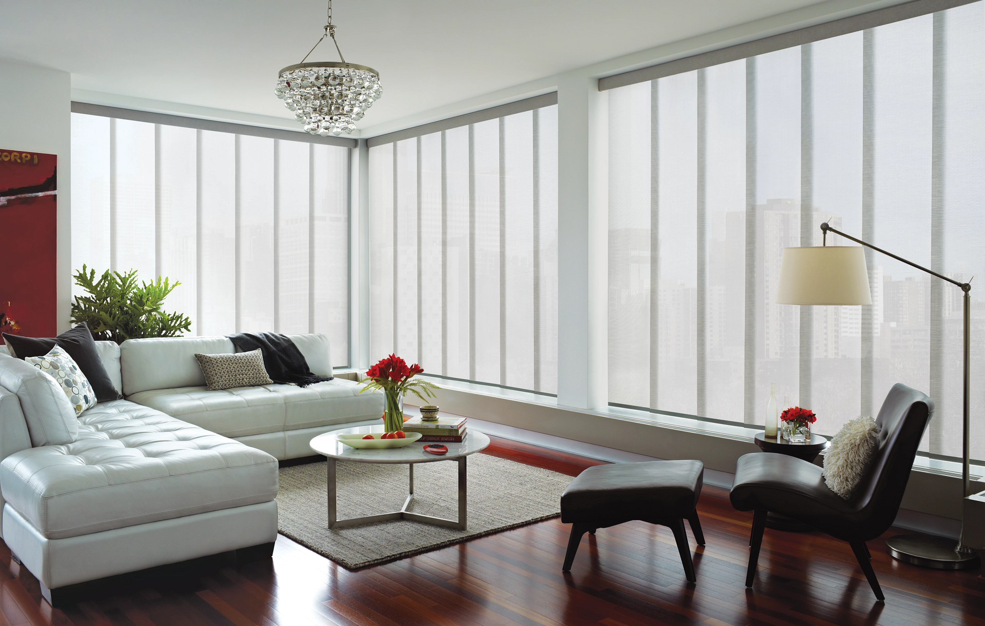A living room with a white sectional couch , chairs , and a lamp.