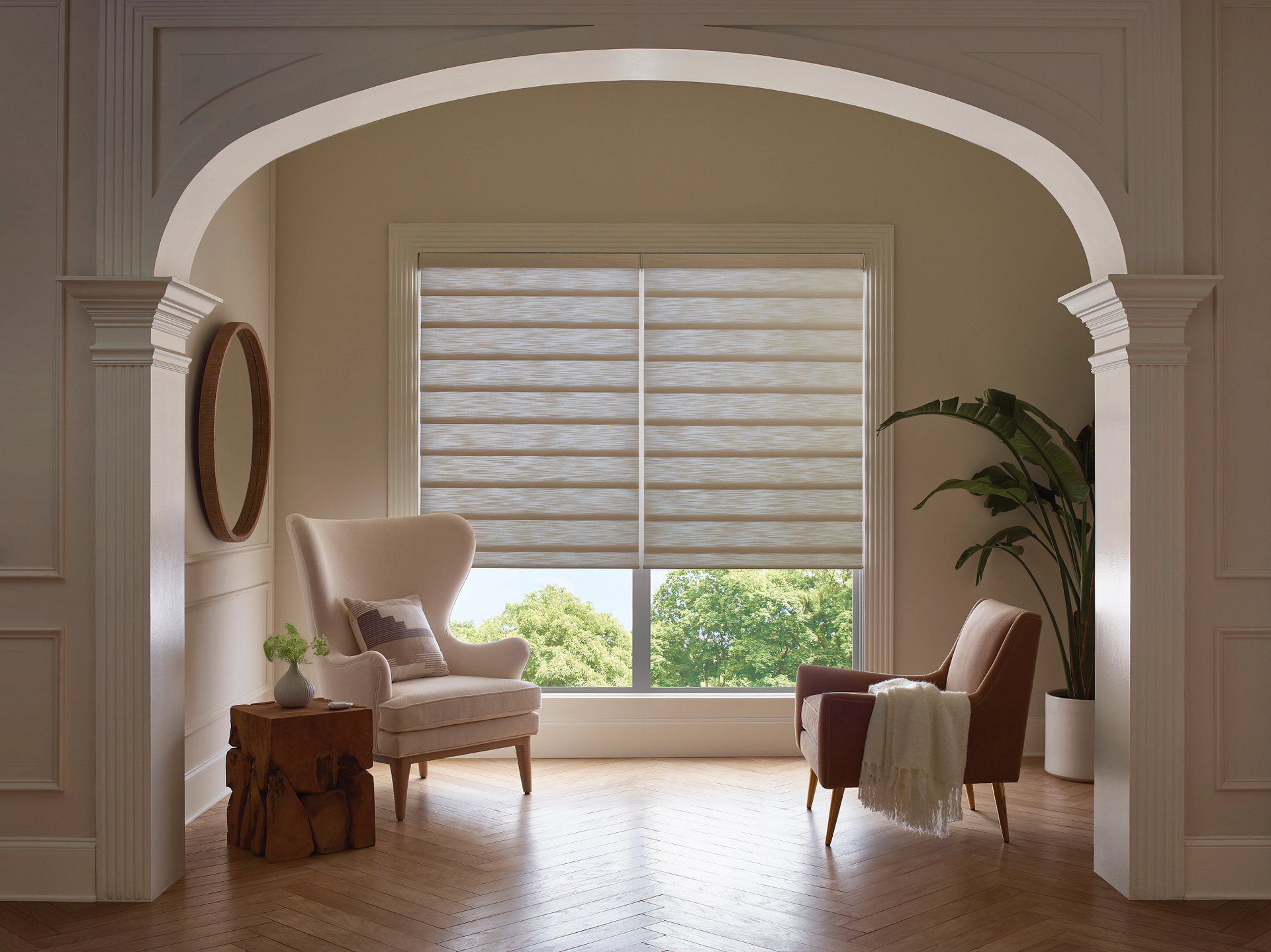 A living room with two chairs and a window with roman shades.