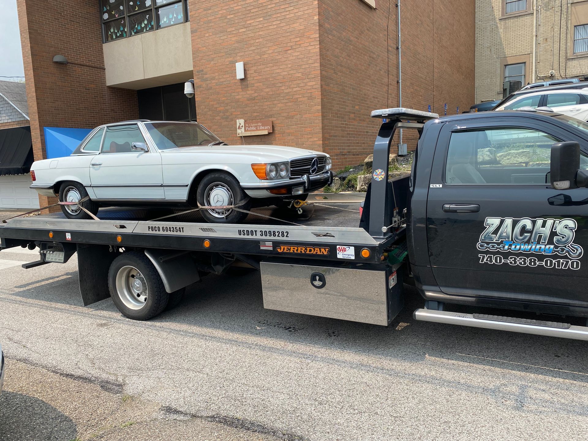 A white car is being towed by a tow truck.