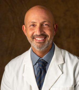 Bald man with a gray beard, wearing a white lab coat, smiling at the camera.