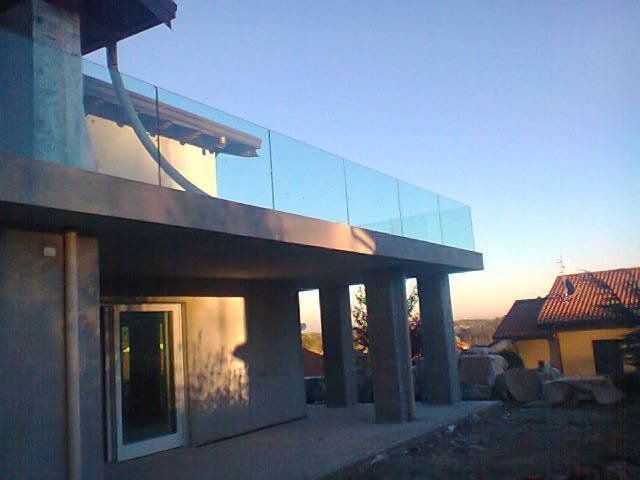 Casa moderna con ringhiera in vetro del balcone; struttura in cemento, cielo sereno.
