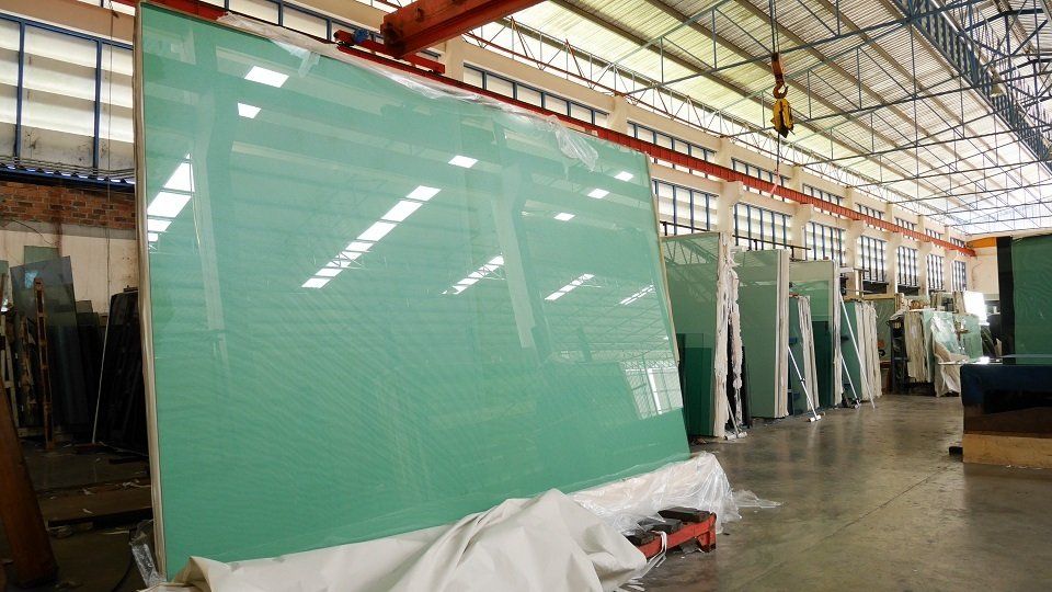 Grandi pannelli di vetro avvolti in una copertura protettiva in un magazzino, sotto una gru.