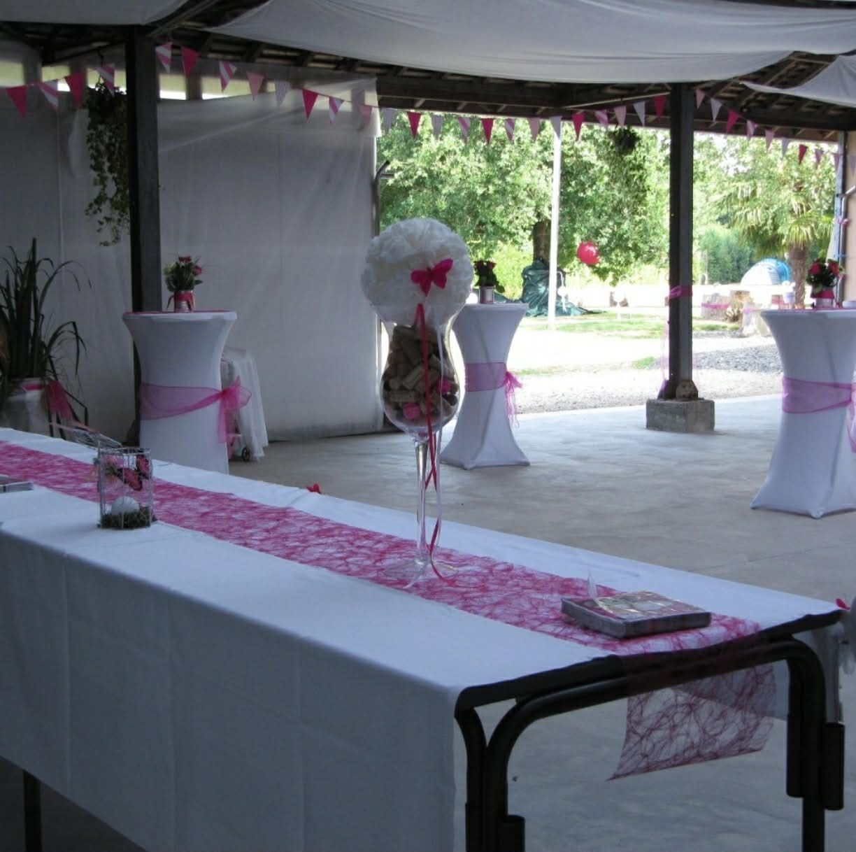 Tente extérieure décorée pour un événement, avec nappes blanches, chemins de table roses et grands centres de table floraux.