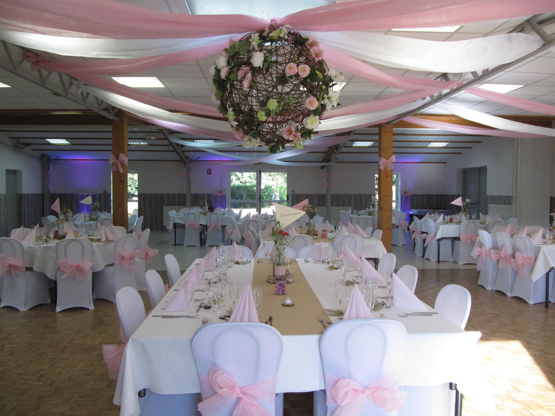 Salle de réception de mariage décorée avec des housses de chaises blanches, des draperies rose.