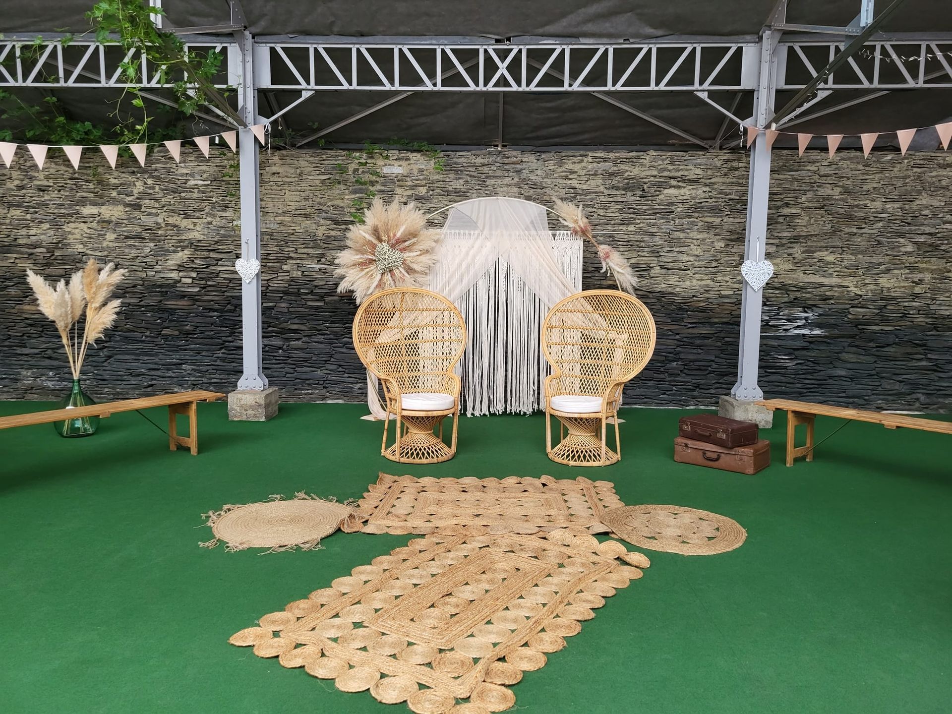 Aménagement d'un événement en extérieur avec des chaises en osier, une décoration en paille et un tapis beige.