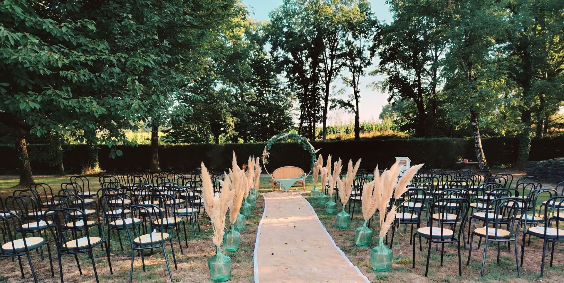 Allée nuptiale en plein air avec chaises blanches et décorations florales roses sous les arbres