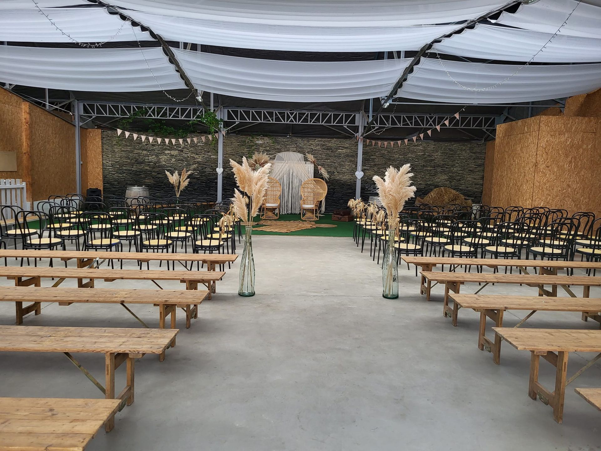 Chapiteau extérieur avec des rangées de bancs en bois faisant face à une scène décorée de compositions florales beiges