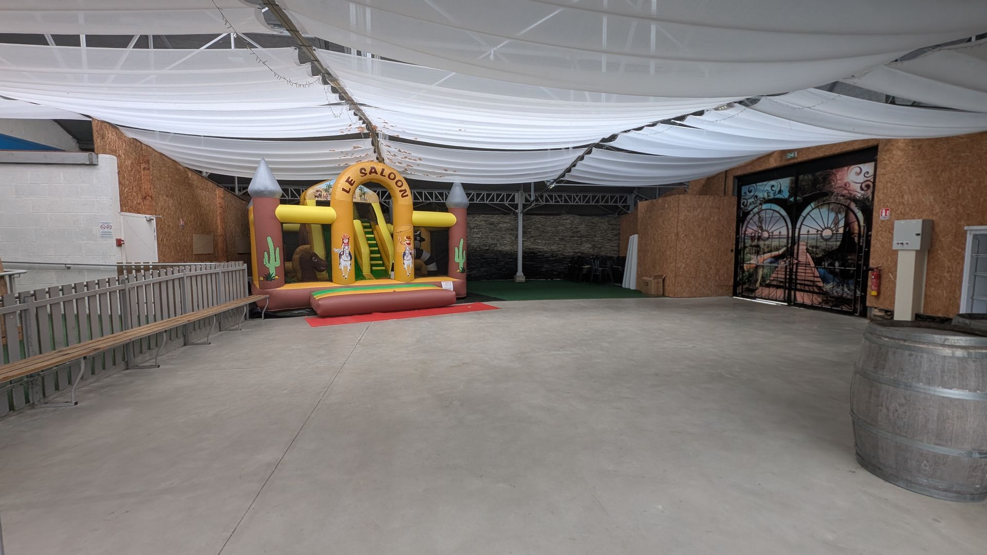Espace événementiel intérieur avec un petit château gonflable jaune et rouge sous un plafond drapé