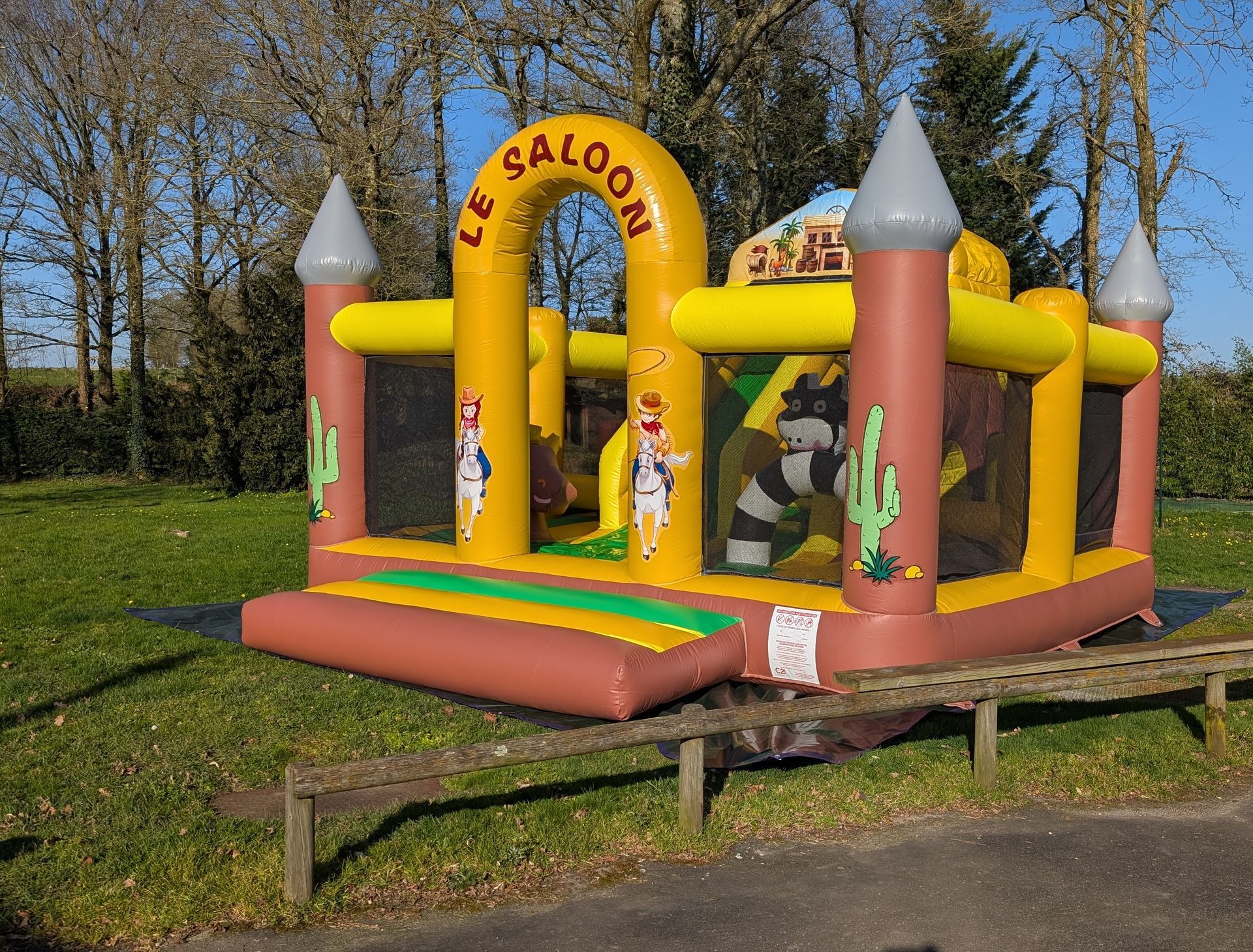 Château gonflable jaune et rose dans un parc, avec des enfants qui jouent à l'intérieur par une journée ensoleillée