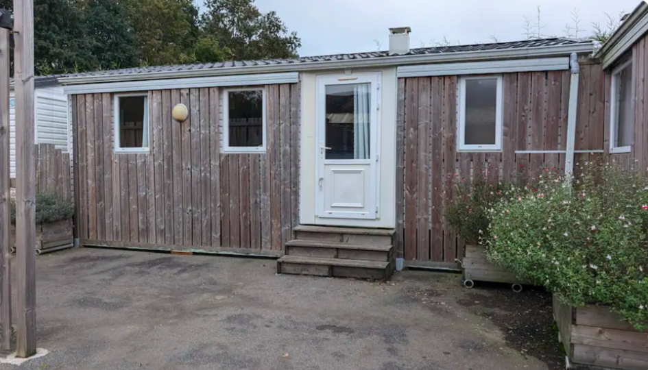 Mobil-home en bois avec porte d'entrée blanche et petites marches, vu depuis une allée pavée.