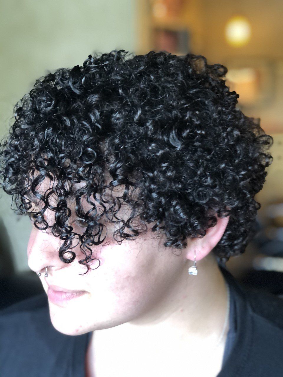 A woman with curly hair is wearing a black shirt and earrings