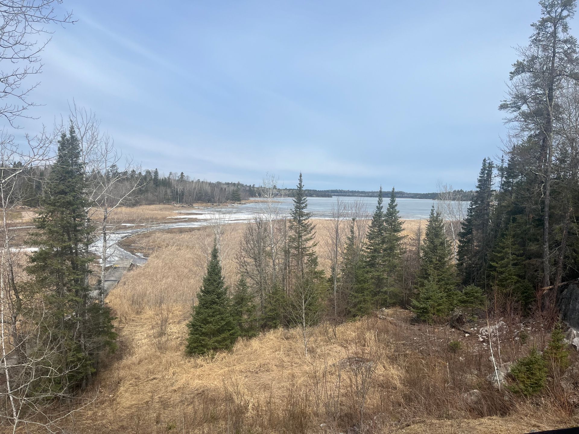 River valley with evergreens, dry grasses, and a distant lake under a pale blue sky