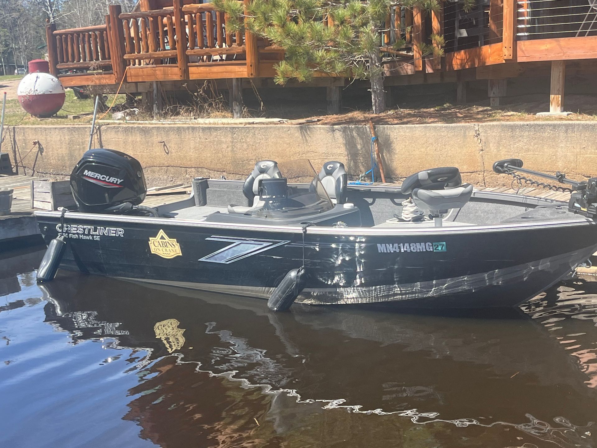 Black fishing boat on calm water beside a dock, with wooden railings and trees in the background.
