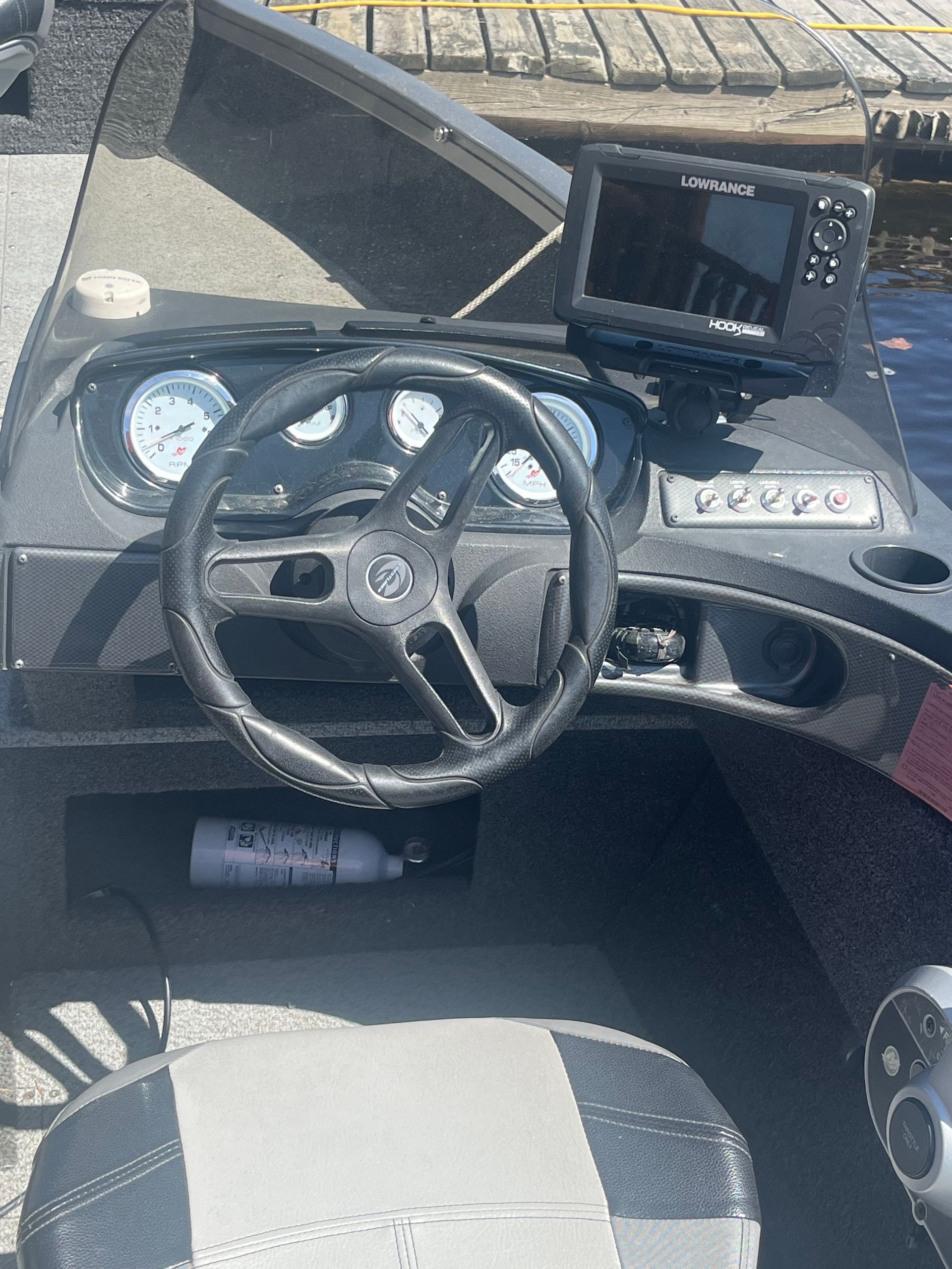 Boat helm with steering wheel, gauges, and mounted display in a gray cockpit seat area