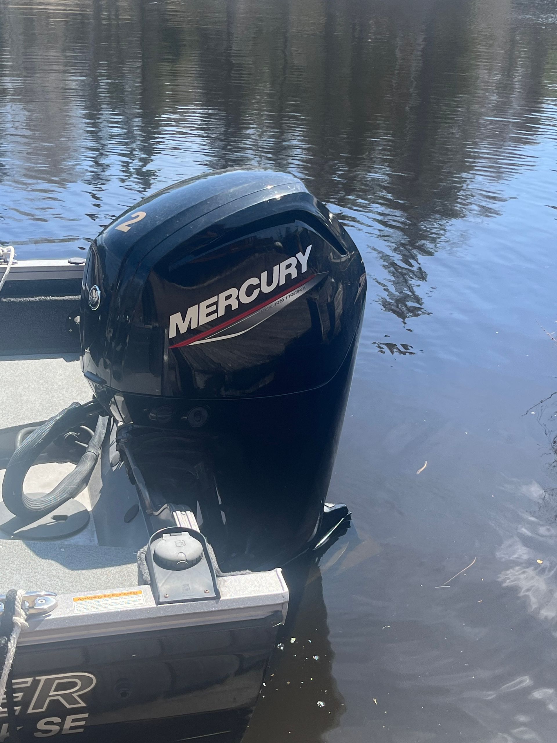 Mercury outboard motor on a boat at the water’s edge, reflecting trees in calm water