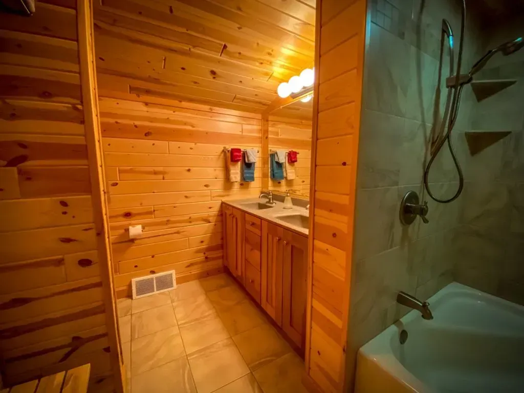 A bathroom in a log cabin with two sinks , a tub and a shower.
