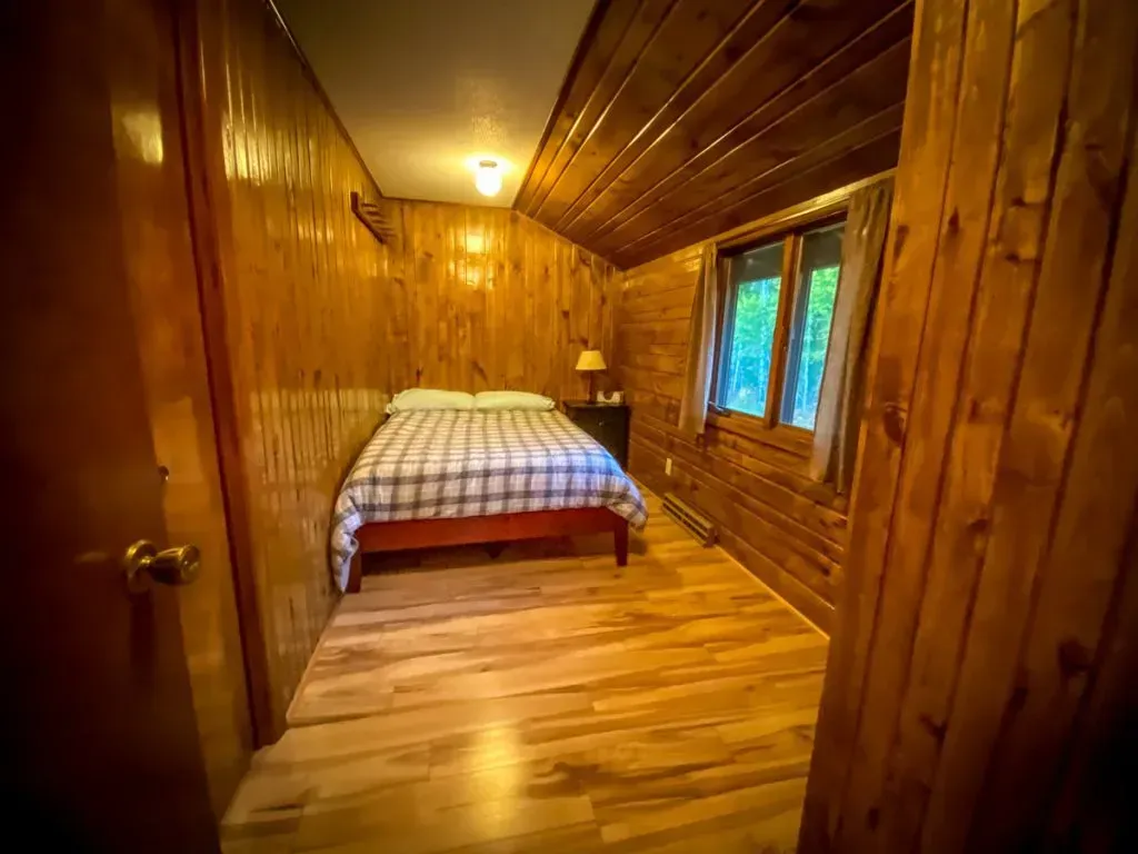 A bedroom in a log cabin with a bed and two windows.