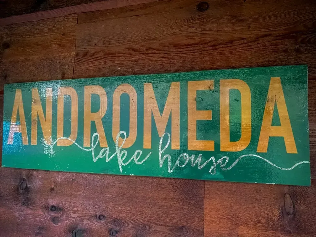 A sign on a wooden wall that says `` andromeda lake house ''.