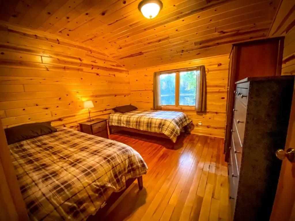 A bedroom in a log cabin with two beds and a dresser.