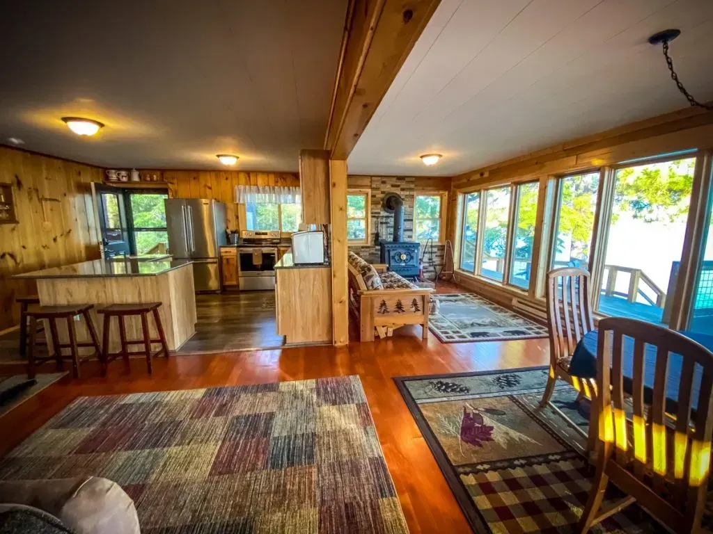 A living room in a cabin with a lot of windows and a rug.
