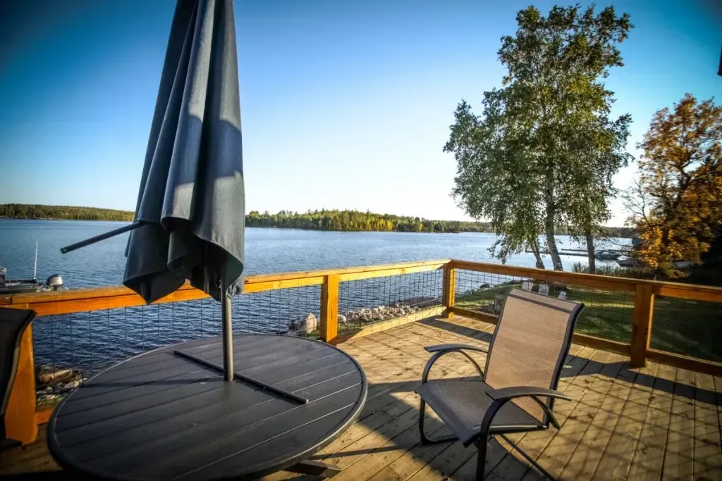 A patio with a table and chairs and an umbrella overlooking a lake.