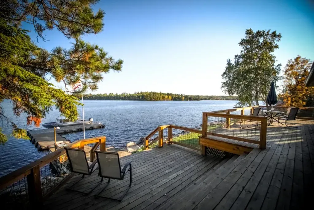 A wooden deck overlooking a lake with chairs and umbrellas