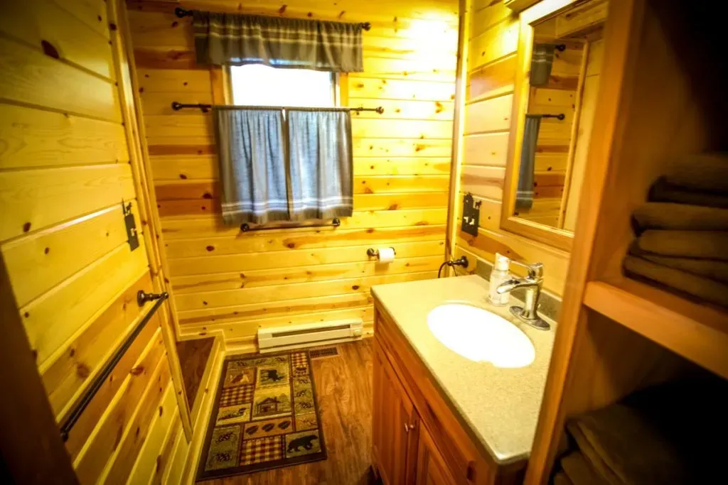 A bathroom in a log cabin with a sink , mirror and window.