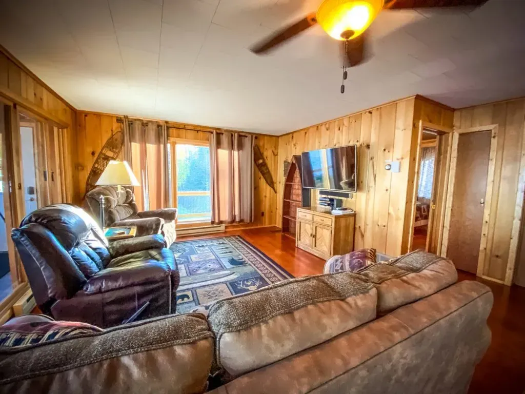 A living room with a couch , chair , television and ceiling fan.