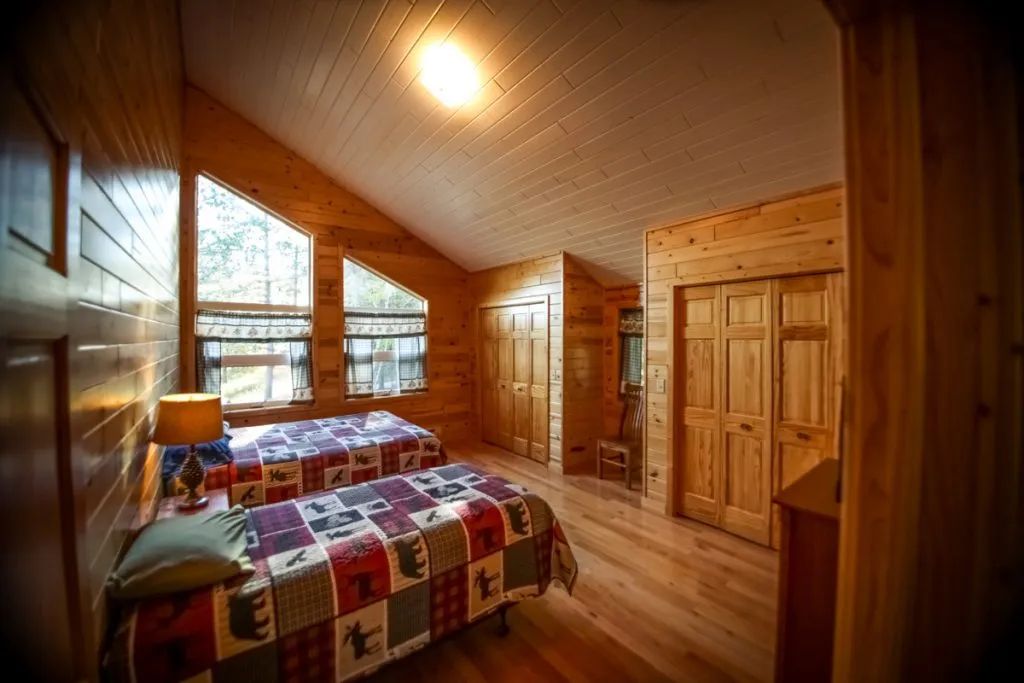 A bedroom in a log cabin with two beds and a dresser.
