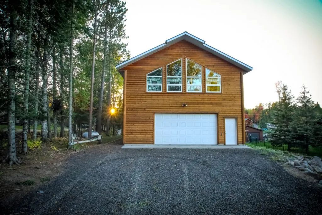 A wooden garage with a white garage door is surrounded by trees