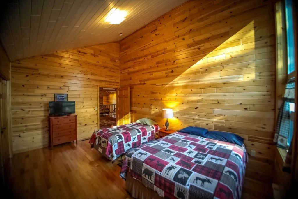A bedroom in a log cabin with two beds and a television.