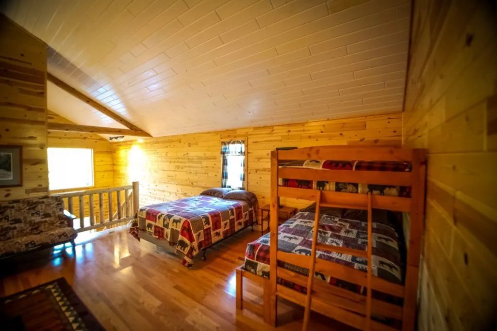 A bedroom in a log cabin with two beds and a bunk bed.