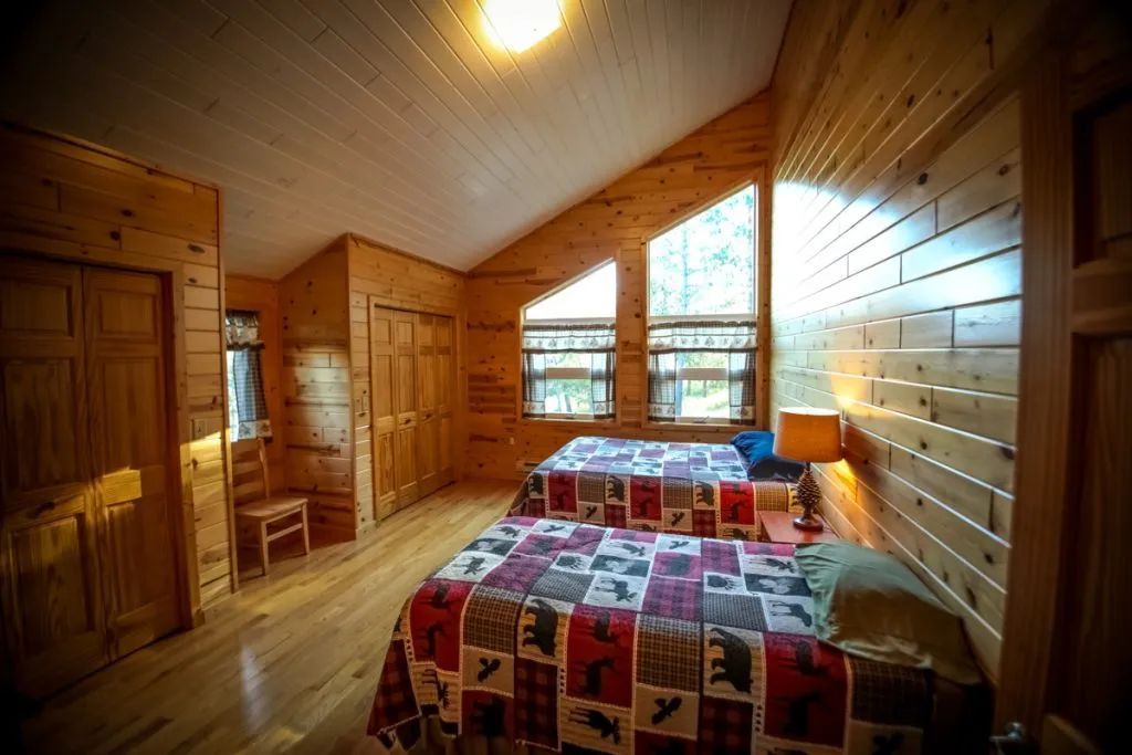 A bedroom in a log cabin with two beds and lots of windows.