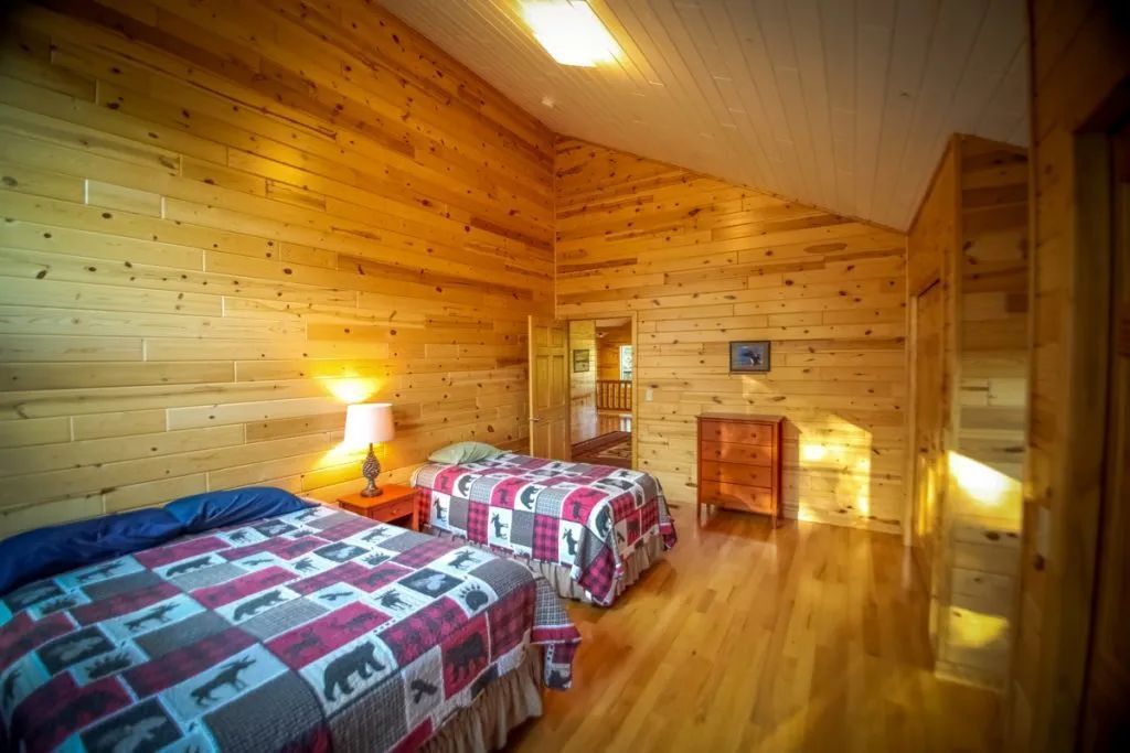 A bedroom in a log cabin with two beds and a dresser.